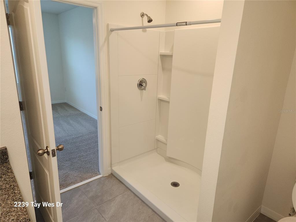 A bathroom features a white walk-in shower with built-in shelving and a gray tiled floor — 2239 TAY WES DRIVE, ST CLOUD, FL
