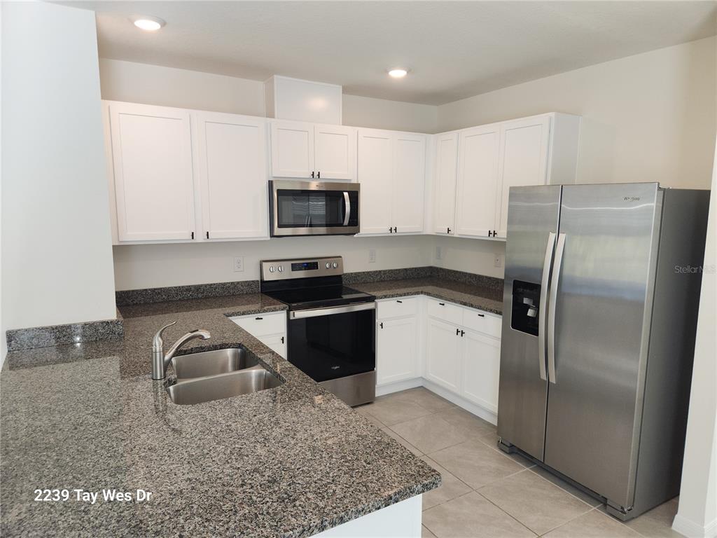 A kitchen features white cabinets, granite countertops, stainless steel appliances, and tile flooring — 2239 TAY WES DRIVE, ST CLOUD, FL