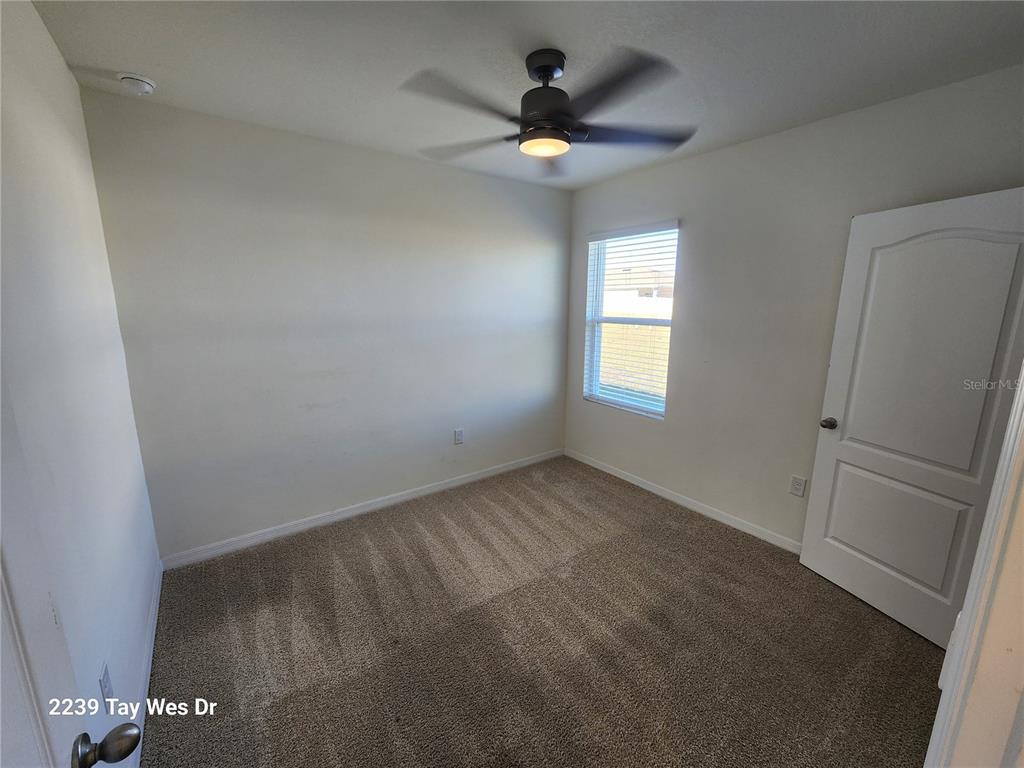 An empty bedroom features beige carpet, white walls, a ceiling fan, and a window — 2239 TAY WES DRIVE, ST CLOUD, FL