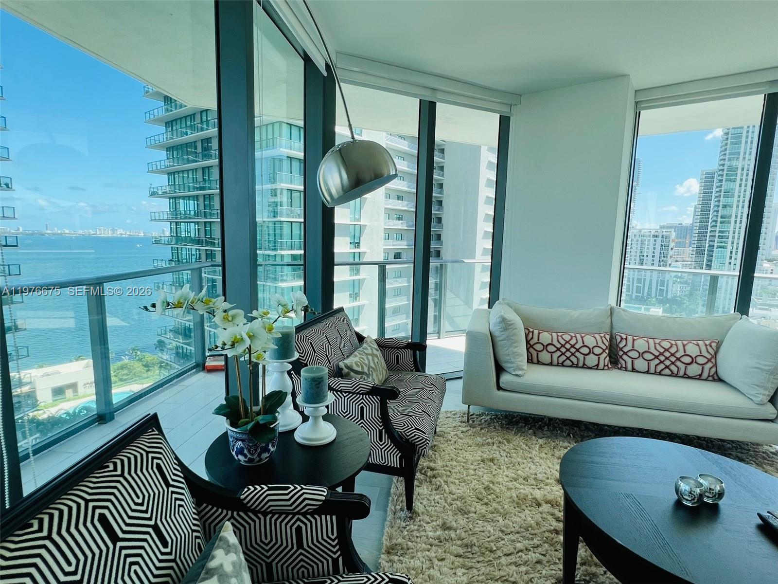 A living room features floor-to-ceiling windows with water views, patterned chairs, and a white sofa — 501 NE 31st St # 1606, Miami FL 33137, MIAMI, FL