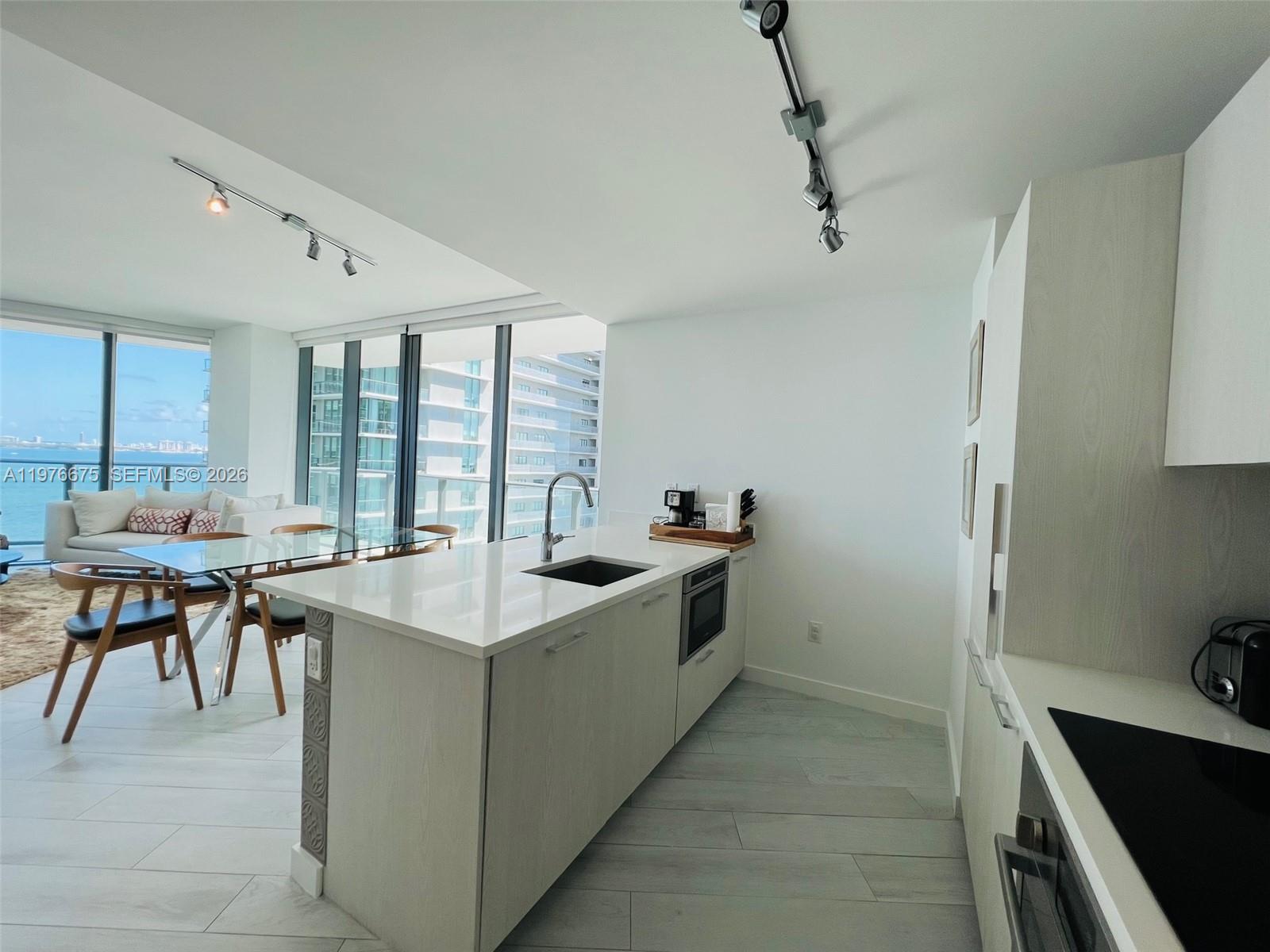 A modern kitchen features a white island with a sink, light wood cabinetry, and dining area — 501 NE 31st St # 1606, Miami FL 33137, MIAMI, FL