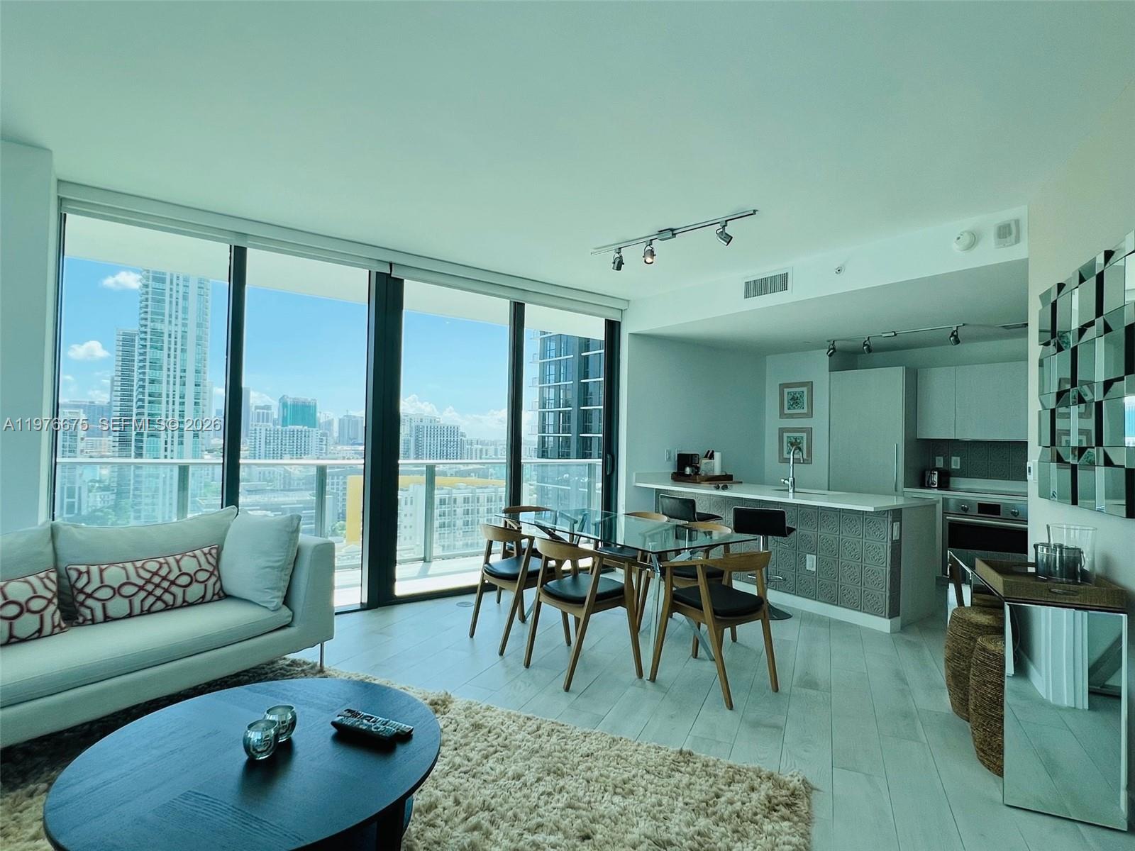 A modern living and dining area features floor-to-ceiling windows with a city skyline view — 501 NE 31st St # 1606, Miami FL 33137, MIAMI, FL