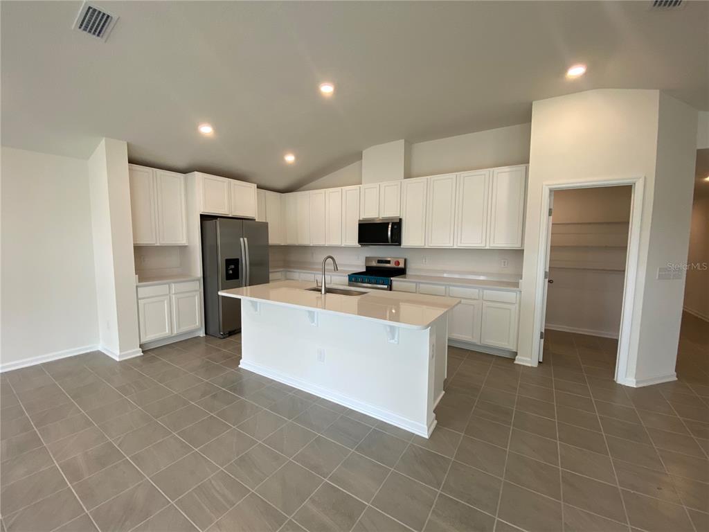 A modern kitchen features white cabinetry, a central island, stainless steel appliances, and tile flooring — 42 CAMELLIA STREET, PALM COAST, FL
