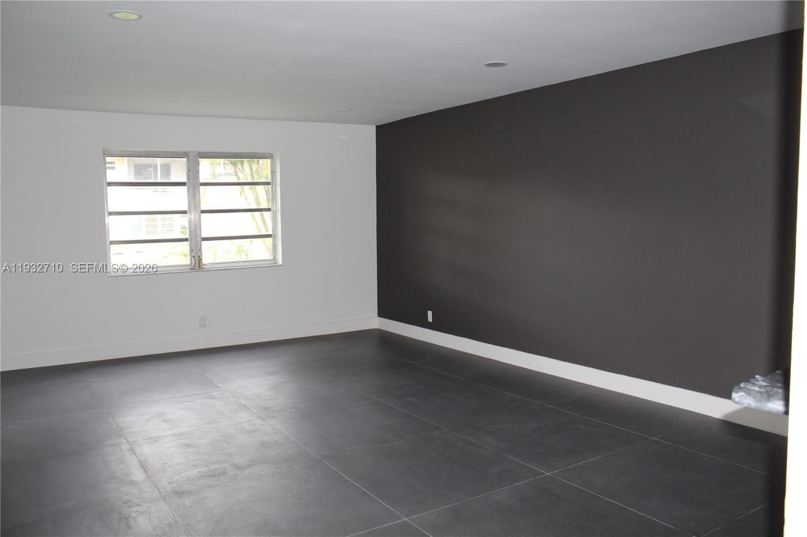 An empty room features dark gray floor tiles, a dark accent wall, and a white window — 5140 SW 40th Ave # 3C, Dania Beach FL 33314, DANIA BEACH, FL