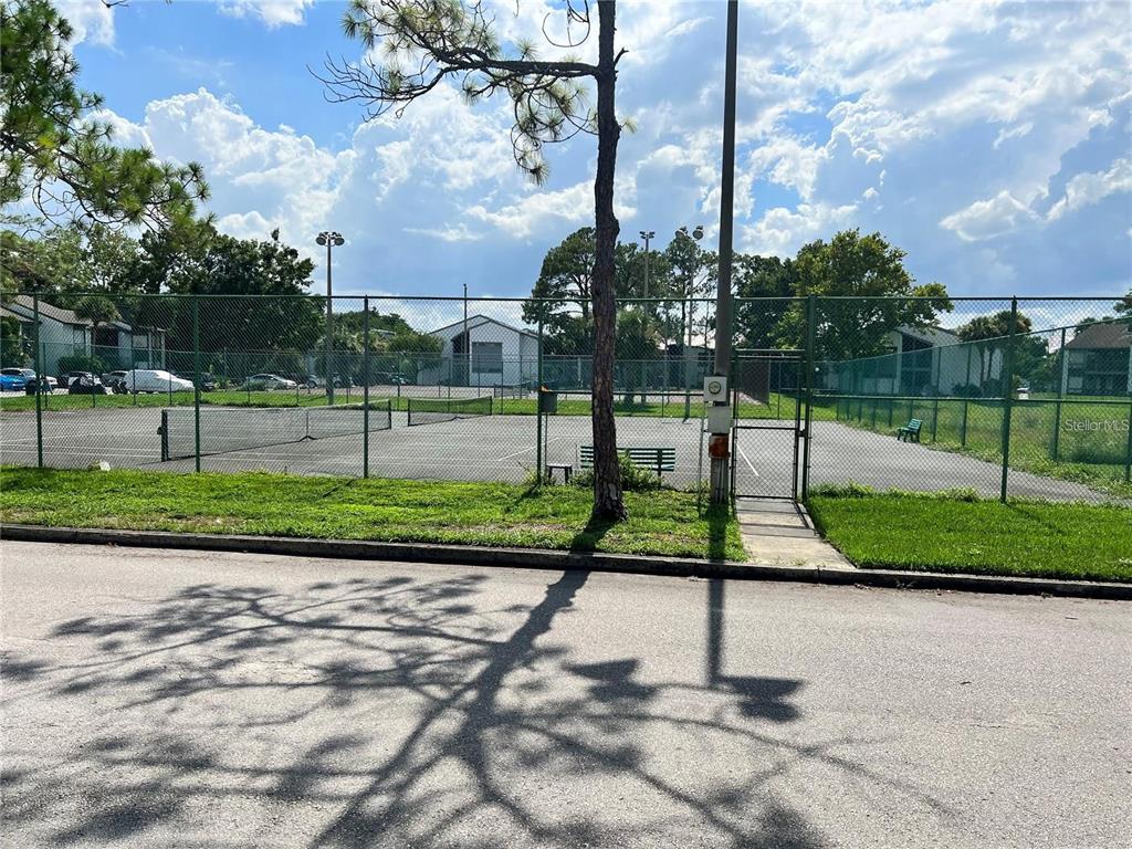 A fenced-in tennis court sits next to a paved road under a cloudy blue sky — 2538 CITRUS CLUB LANE UNIT 105, ORLANDO, FL