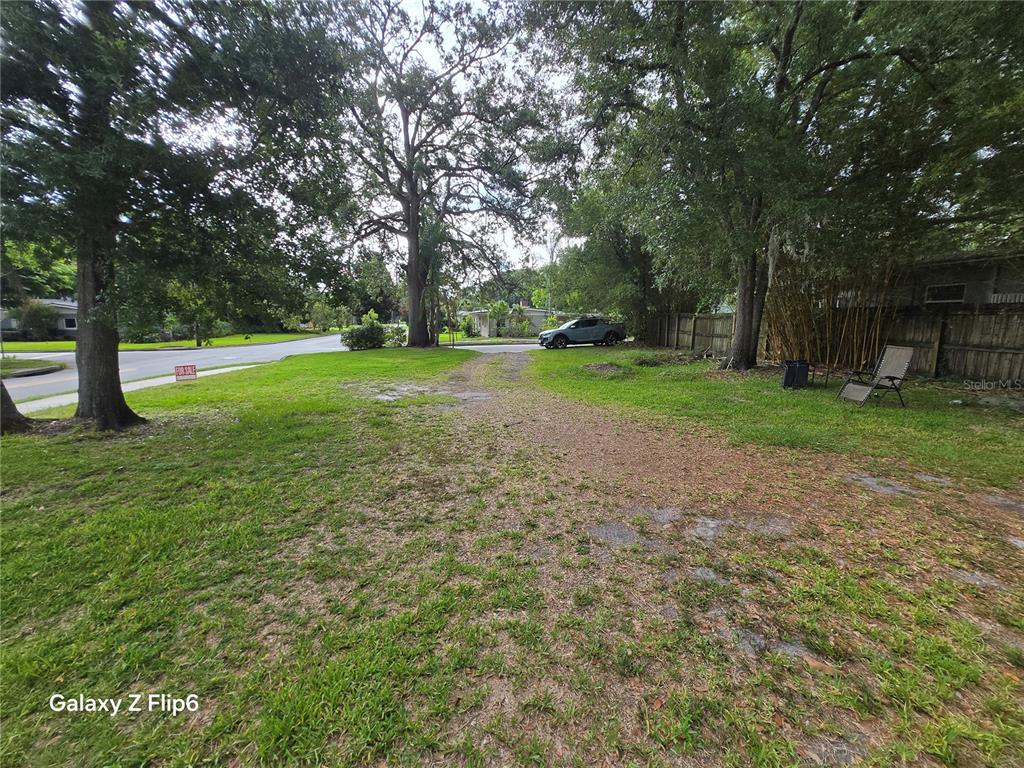 A grassy, tree-lined vacant lot with a gravel driveway and a parked vehicle — HELEN AVENUE, ORLANDO, FL