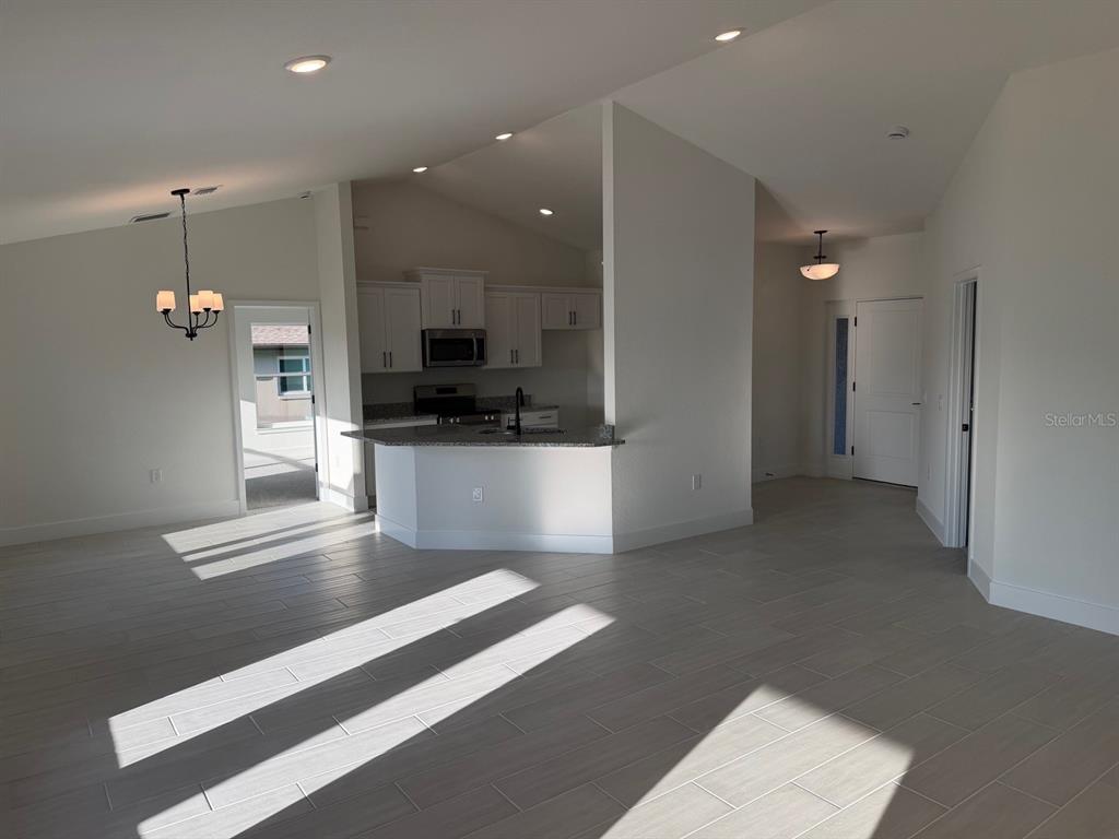 An open-concept kitchen with white cabinets and a breakfast bar overlooks a tiled living area — 2110 CARPETGREEN STREET, PORT CHARLOTTE, FL