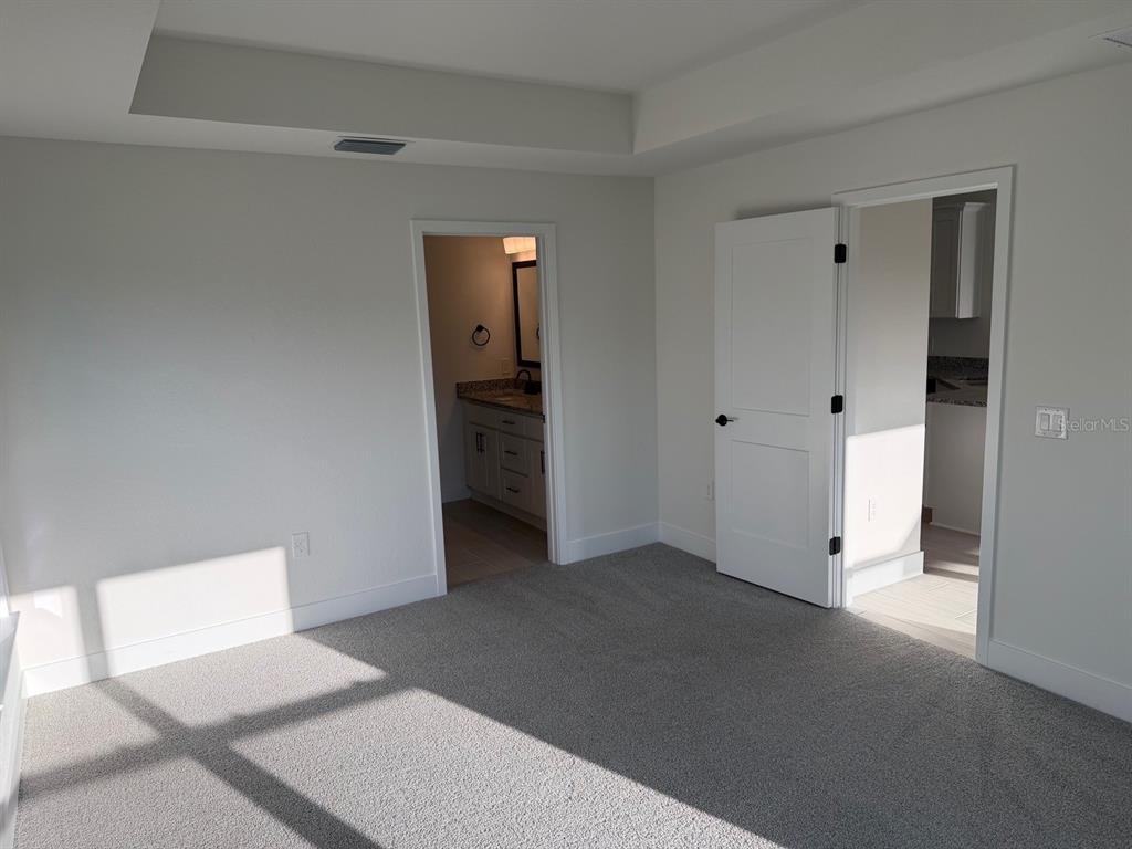 A carpeted bedroom features a tray ceiling, a bathroom doorway, and an open closet door — 2110 CARPETGREEN STREET, PORT CHARLOTTE, FL
