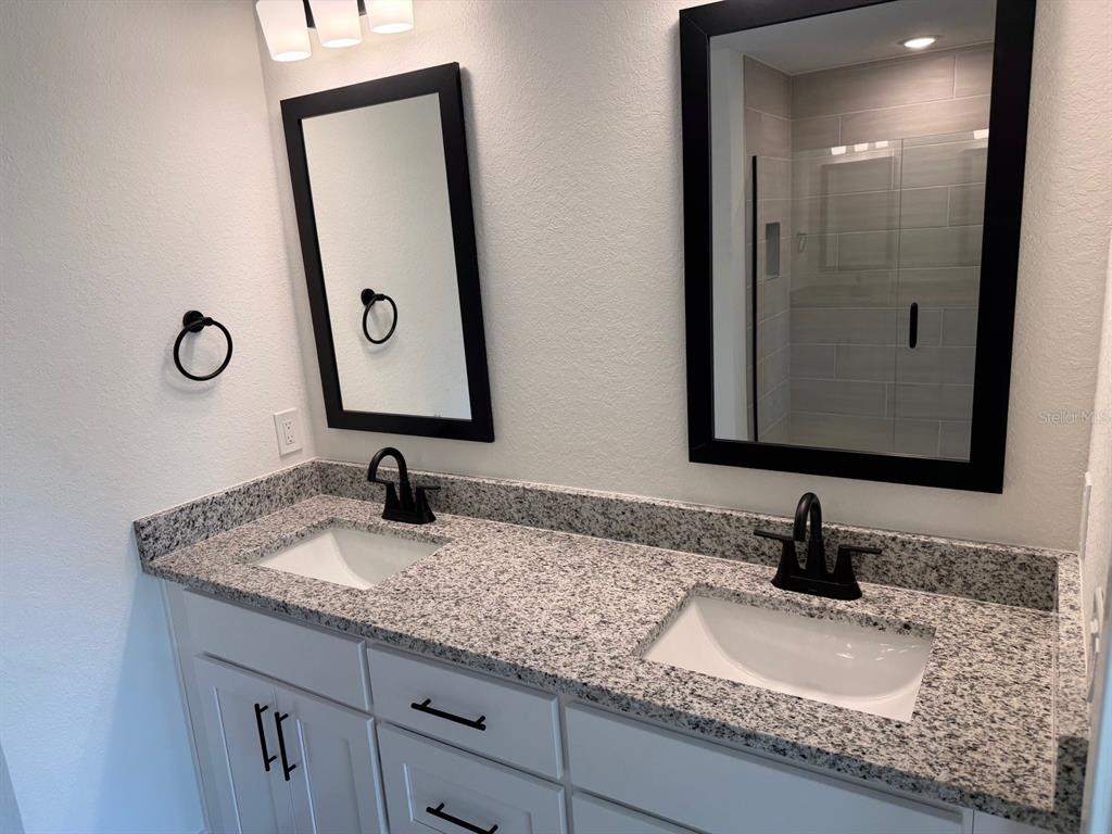 A bathroom features a double vanity with white cabinets, granite countertops, and two black-framed mirrors — 2110 CARPETGREEN STREET, PORT CHARLOTTE, FL