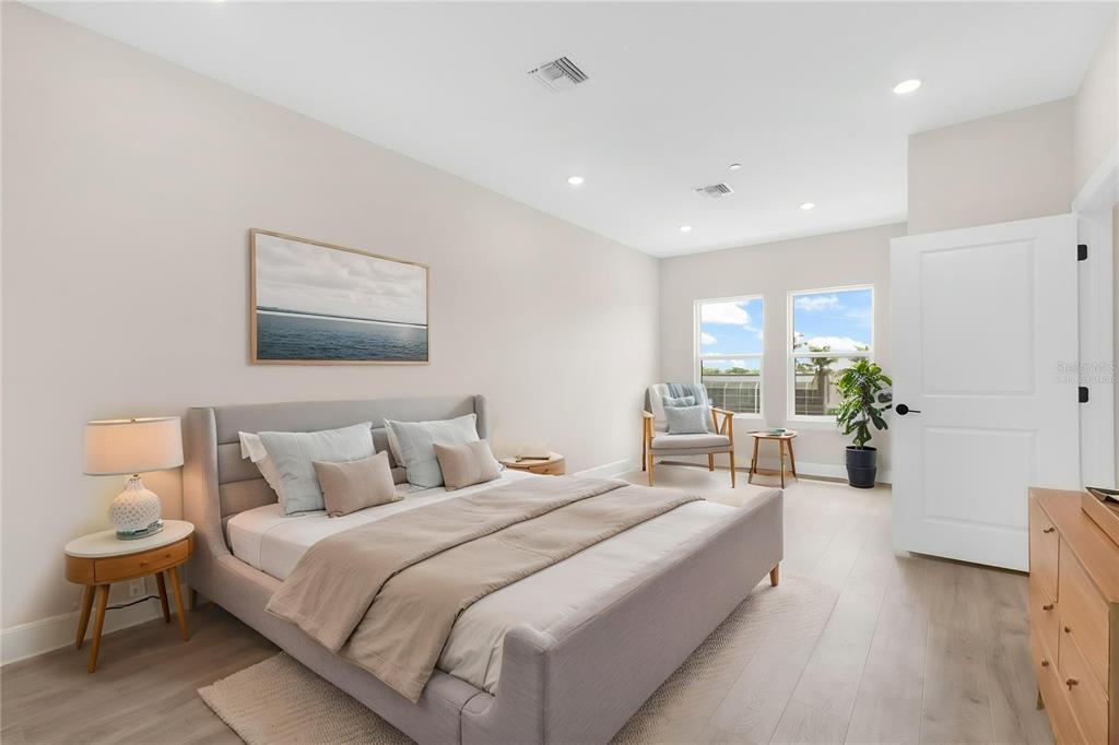 A modern bedroom features a gray upholstered bed, light wood flooring, and two large windows — 1617 SEAHAVEN DRIVE UNIT 504, PUNTA GORDA, FL