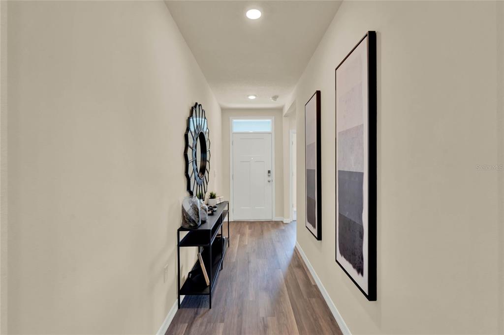 A narrow hallway features wood-look flooring, a black console table, and wall-mounted artwork — 7833 FORREST FOX WAY, LAKELAND, FL