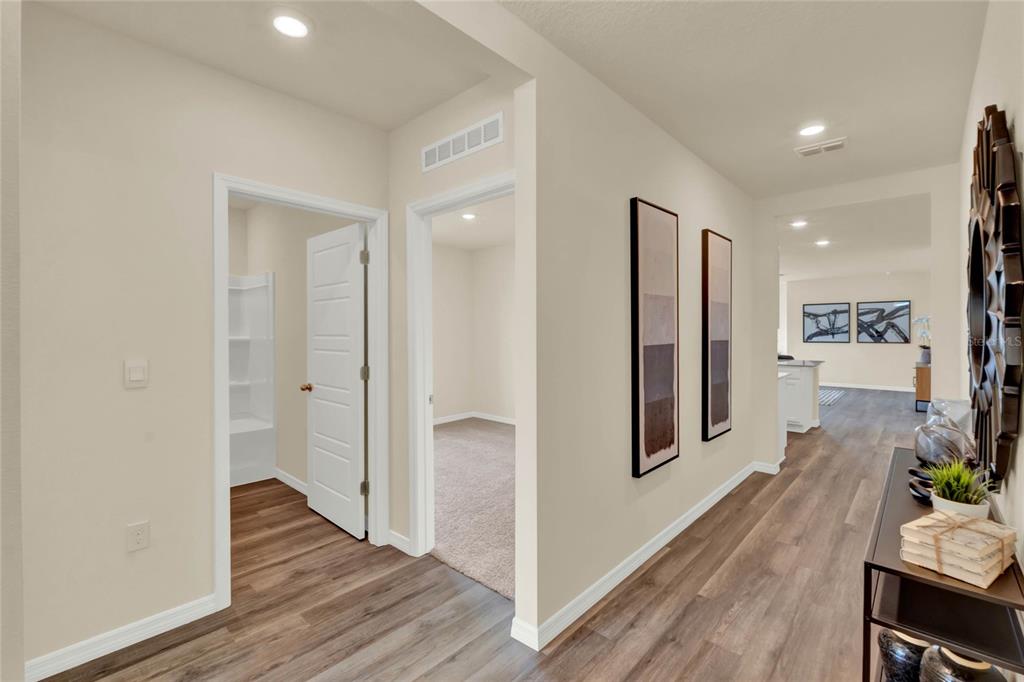 A hallway with wood-look flooring leads past a bedroom and closet toward an open kitchen — 7833 FORREST FOX WAY, LAKELAND, FL