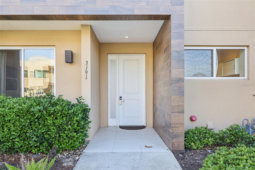 The exterior of a modern home features a white front door and wood-look tile accents — 3191 BRASILIA AVENUE, KISSIMMEE, FL