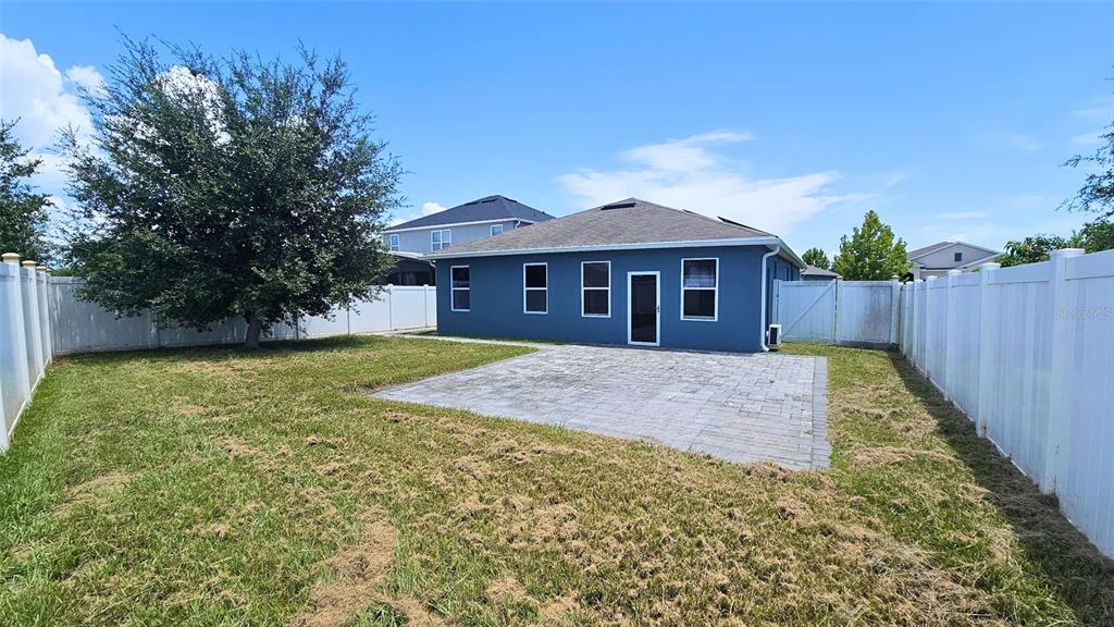 A blue house with a paved patio and a large tree in the fenced backyard — 1724 RANGER HIGHLANDS ROAD, KISSIMMEE, FL