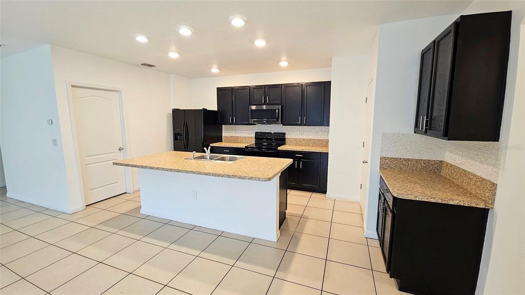 A kitchen features dark cabinets, granite countertops, a central island, and light-colored tile flooring — 1724 RANGER HIGHLANDS ROAD, KISSIMMEE, FL