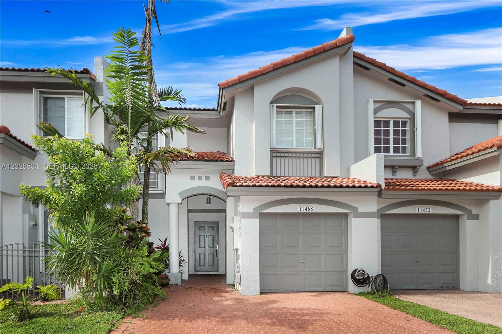 A two-story townhouse features a red tile roof, white stucco walls, and two garage doors — 11468 NW 50th Ter, Doral FL 33178, DORAL, FL