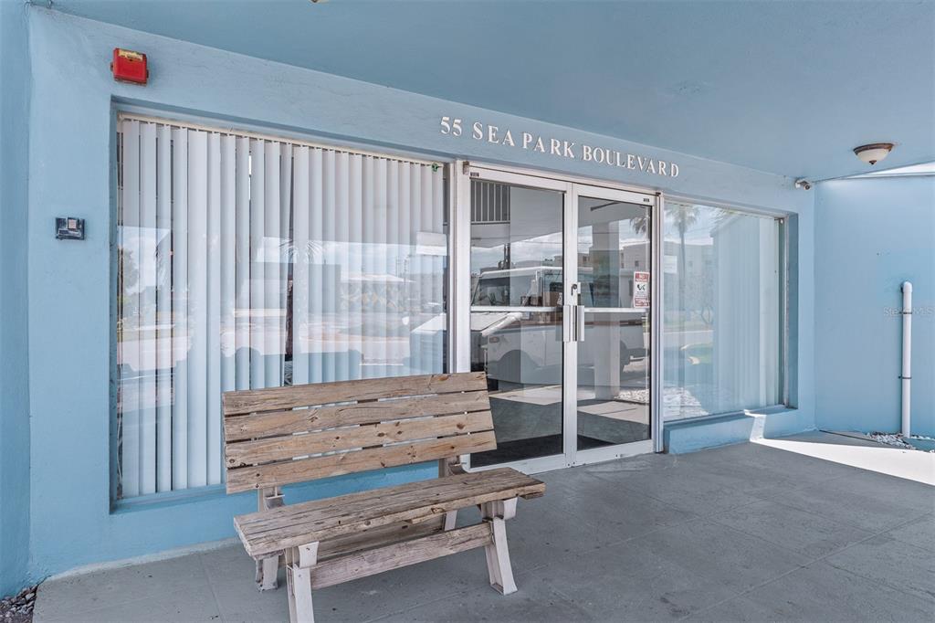 A wooden bench sits on a concrete walkway in front of a blue building entrance — 55 SEA PARK BOULEVARD UNIT 204, SATELLITE BEACH, FL