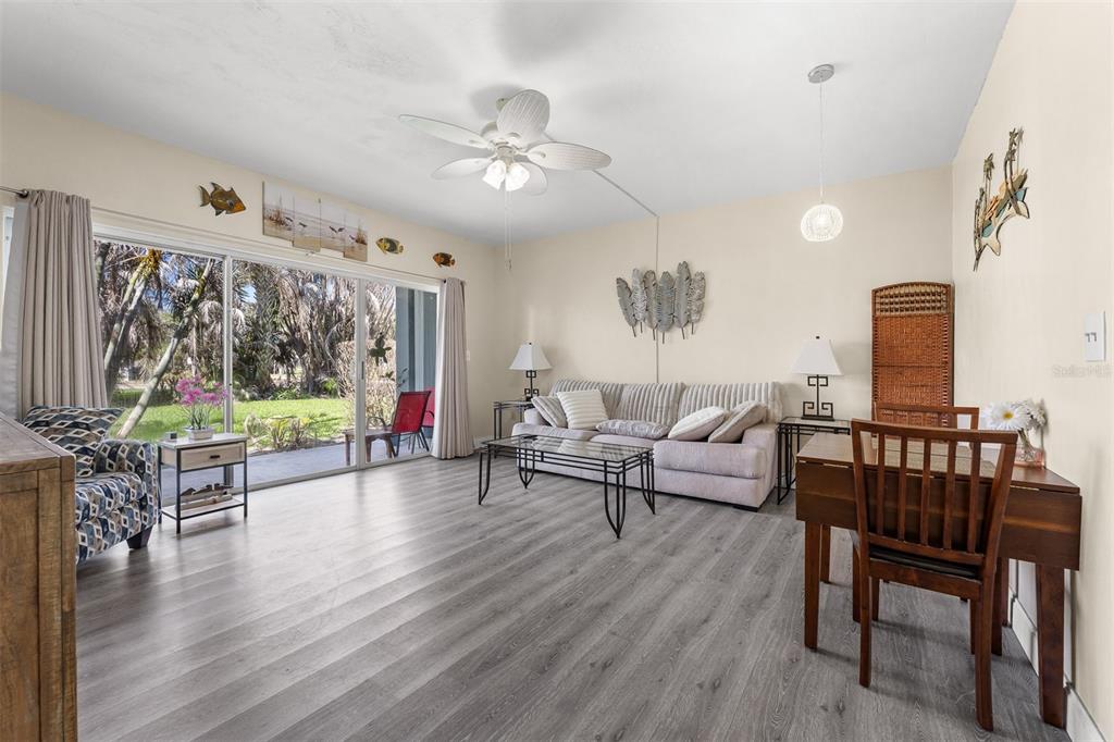 A living room features light wood-look flooring, a ceiling fan, a sofa, and sliding glass doors — 55 SEA PARK BOULEVARD UNIT 204, SATELLITE BEACH, FL