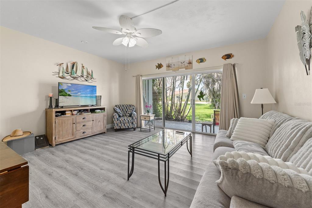 A living room with gray wood-look flooring, a glass coffee table, and a sliding glass door — 55 SEA PARK BOULEVARD UNIT 204, SATELLITE BEACH, FL