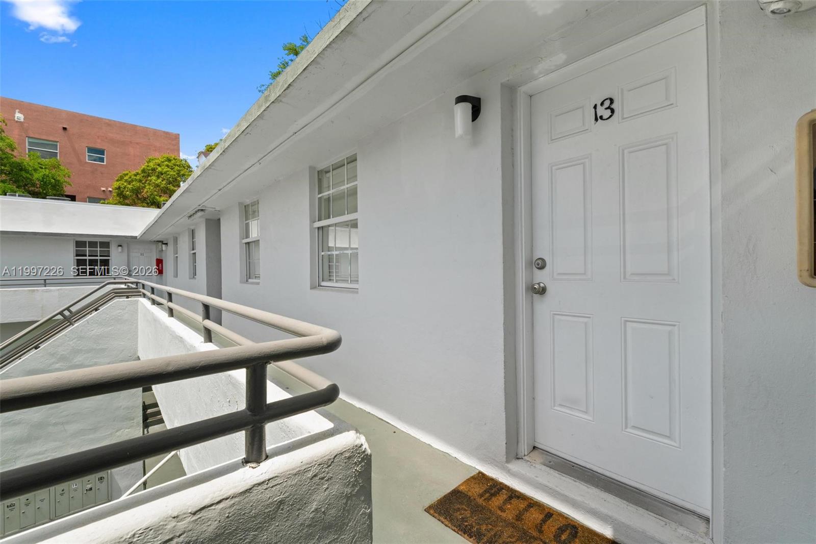 An exterior view of a white apartment building hallway with a door numbered 13 — 541 NE 62nd St # 13, Miami FL 33138, MIAMI, FL
