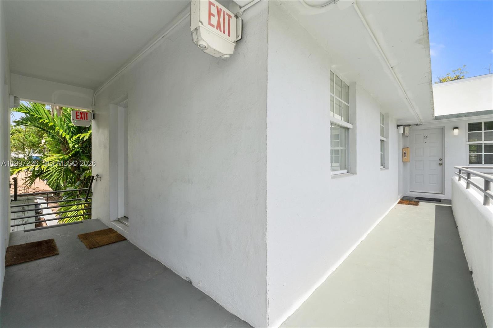 An exterior walkway with white walls, two exit signs, and a door labeled 14 — 541 NE 62nd St # 13, Miami FL 33138, MIAMI, FL
