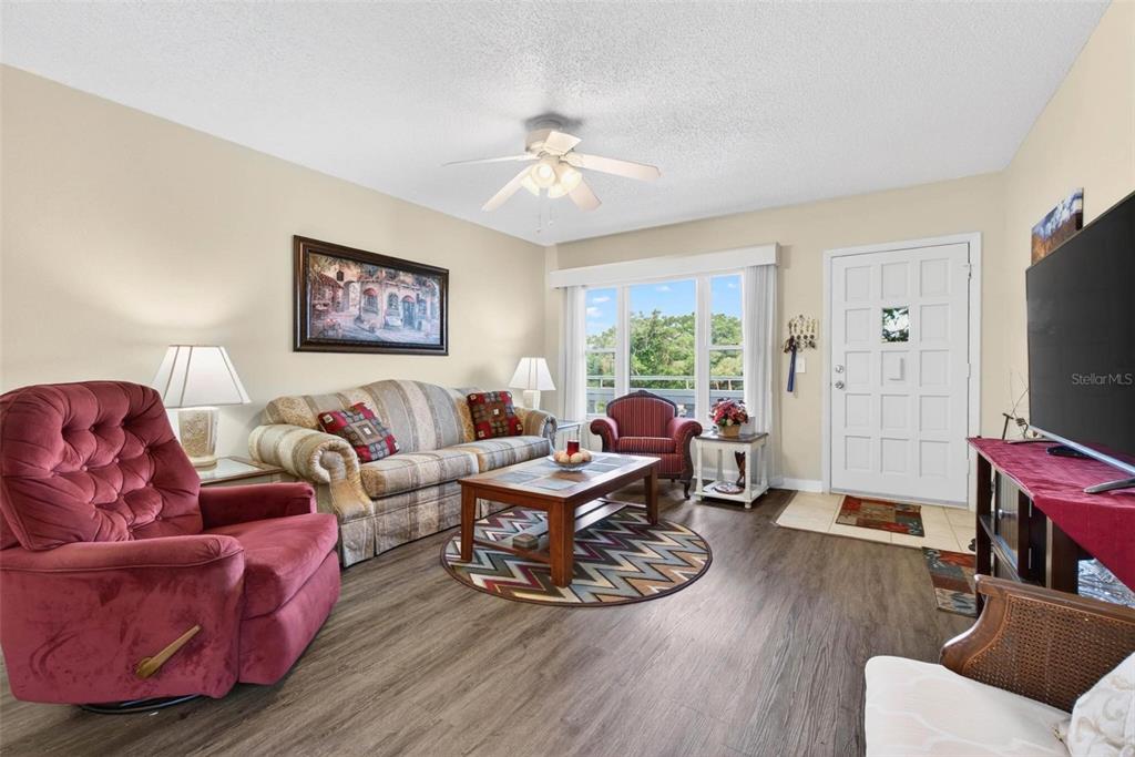 A living room features a red recliner, a patterned sofa, a coffee table, and wood-look flooring — 2461 RHODESIAN DRIVE UNIT 51, CLEARWATER, FL