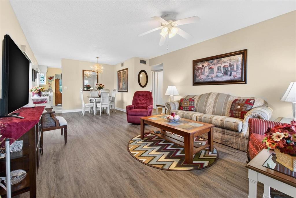 A living room with wood-look flooring, a patterned sofa, a red armchair, and a dining area — 2461 RHODESIAN DRIVE UNIT 51, CLEARWATER, FL