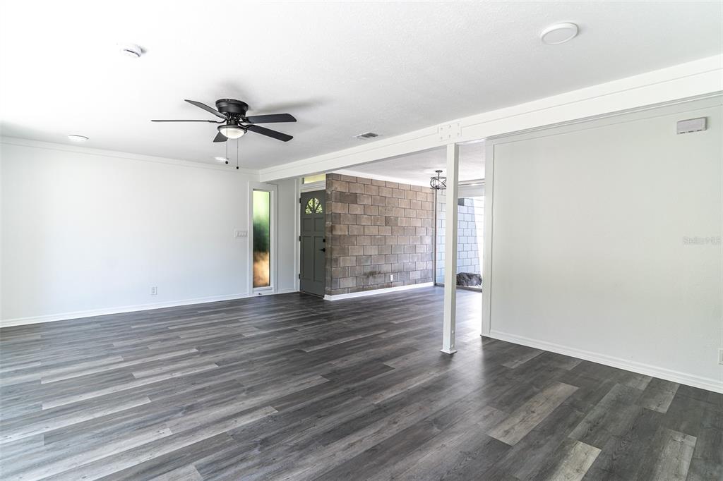 An open living area features gray wood-look flooring, a ceiling fan, and a block wall — 1558 DREXEL AVENUE NE, WINTER HAVEN, FL