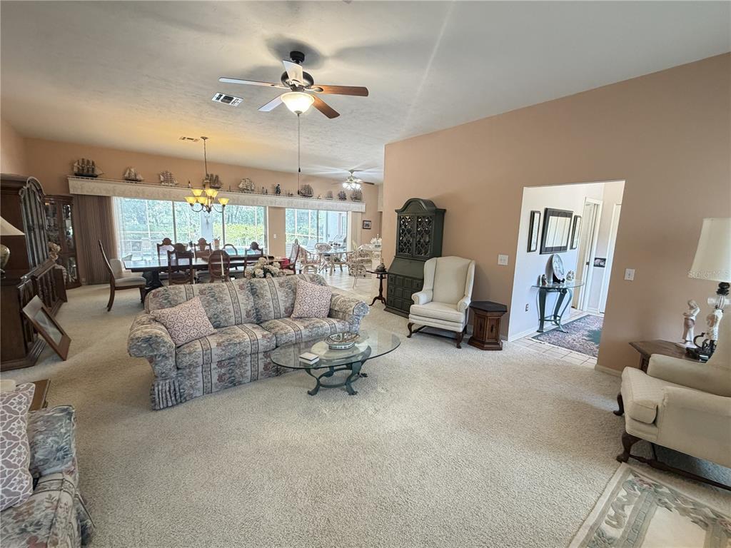 A spacious living room features beige carpeting, a floral sofa, and a dining area beyond — 20620 SW 97TH PLACE, DUNNELLON, FL