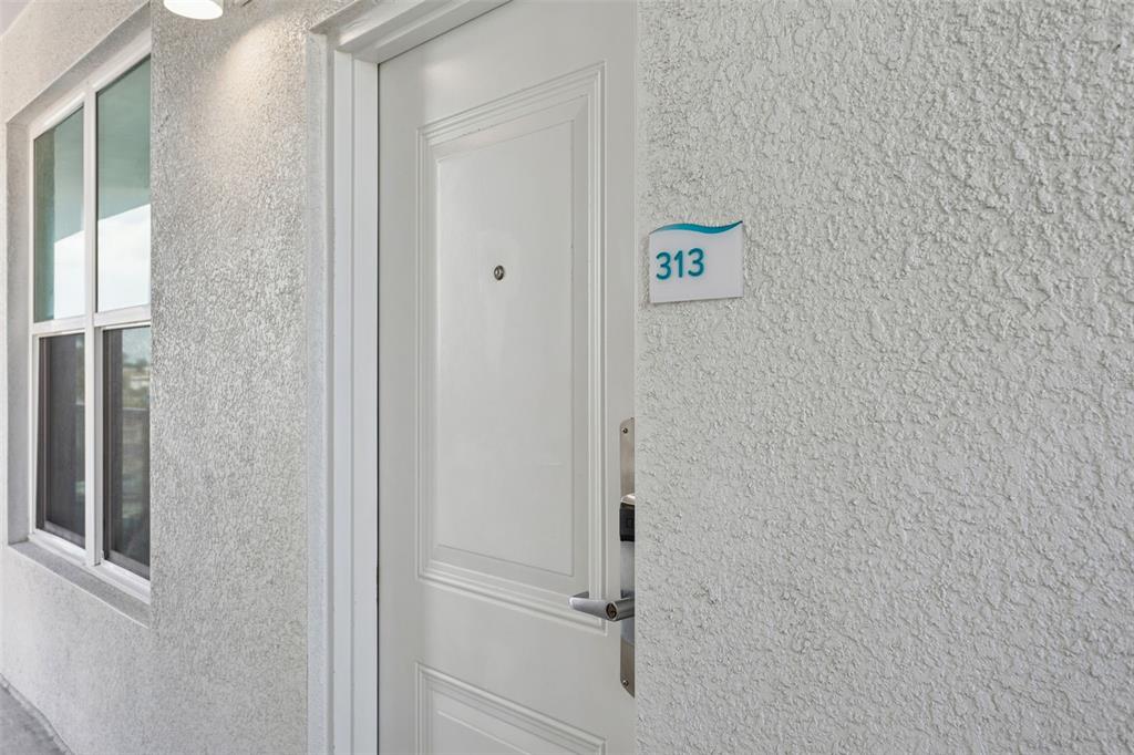A white door with a room number sign labeled 313 is set in a textured wall — 11500 GULF BOULEVARD UNIT 313, TREASURE ISLAND, FL