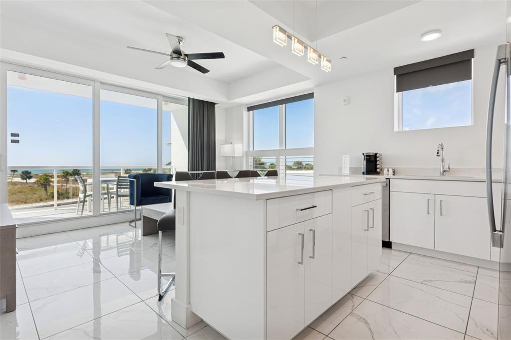 A modern kitchen with white cabinetry and an island overlooks a balcony with ocean views — 11500 GULF BOULEVARD UNIT 313, TREASURE ISLAND, FL