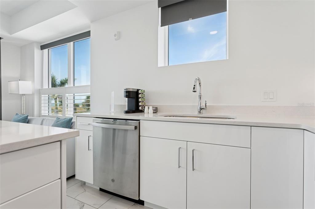 A modern kitchen features white cabinets, stainless steel appliances, and a view of the beach — 11500 GULF BOULEVARD UNIT 313, TREASURE ISLAND, FL
