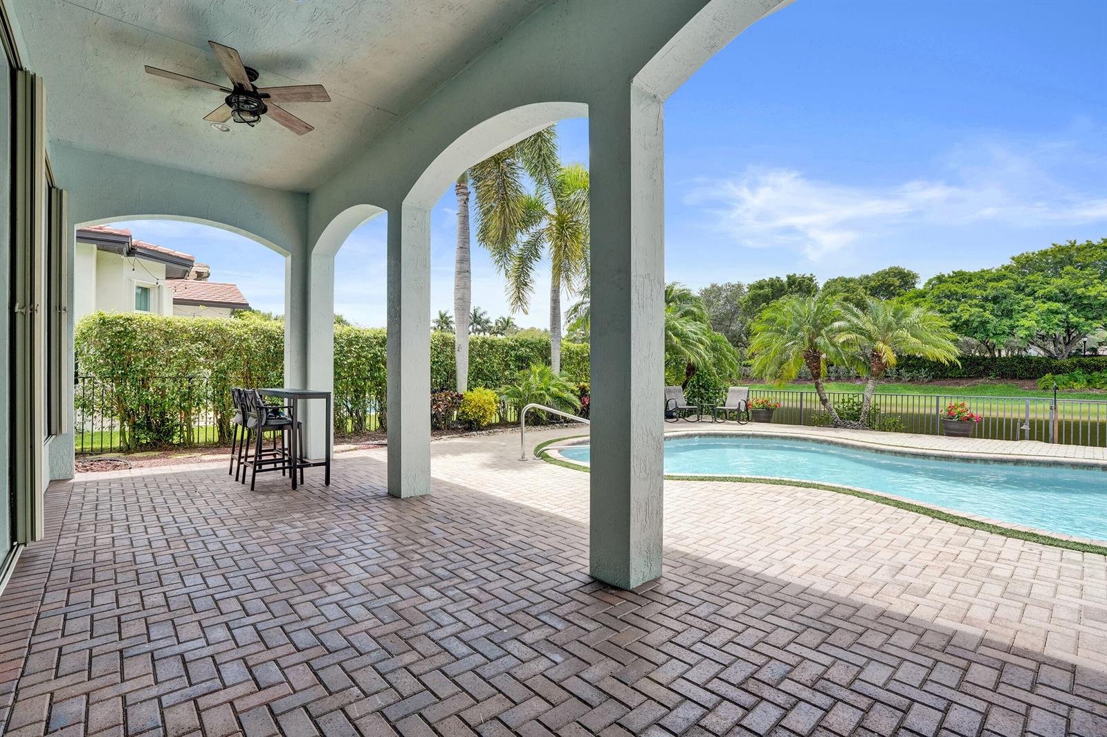 A covered patio features brick pavers, arched columns, a ceiling fan, and a swimming pool — 12370 NW 80th Place, Parkland FL 33076, PARKLAND, FL