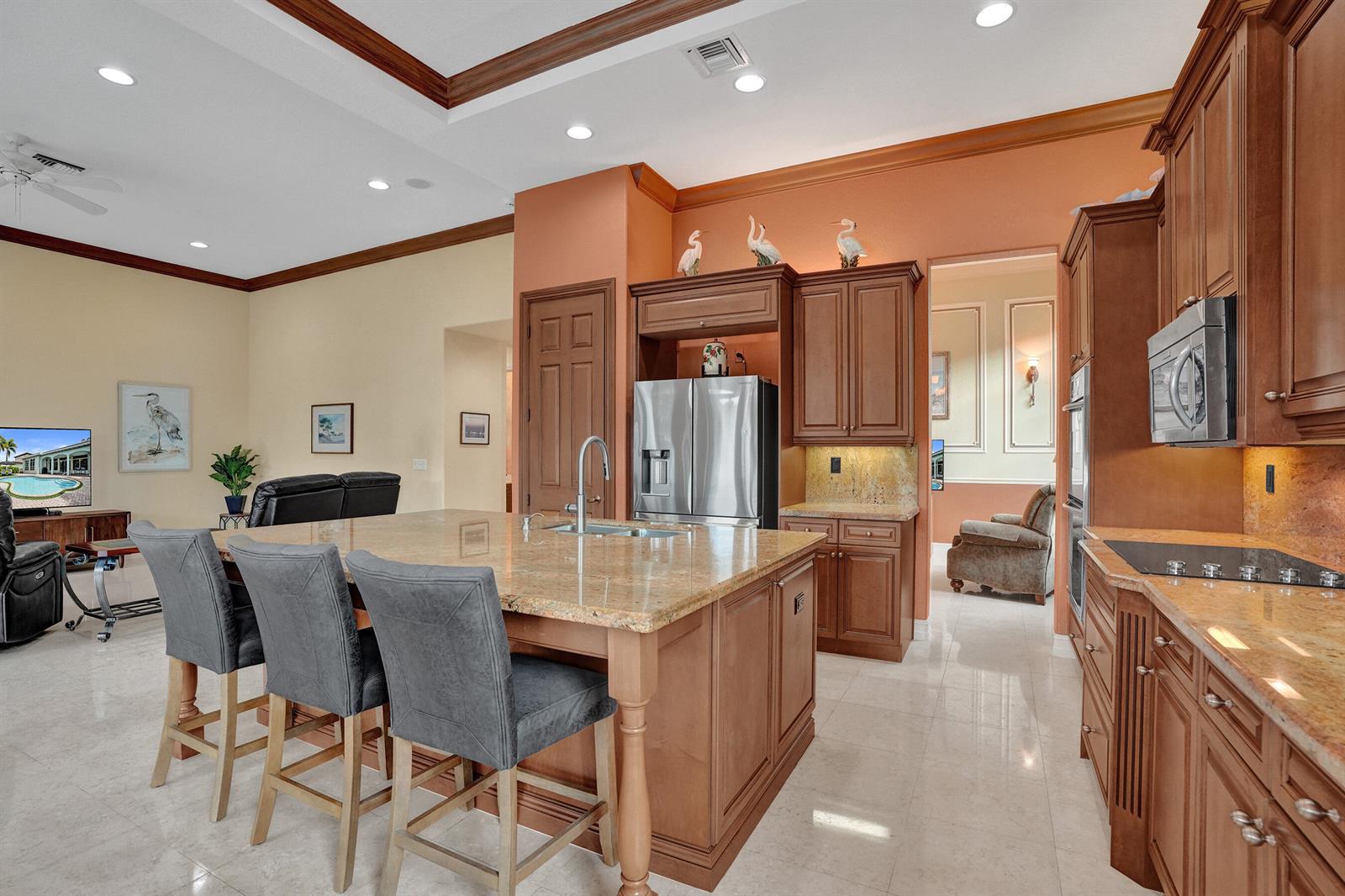 A kitchen features a granite-topped island, wooden cabinetry, stainless steel appliances, and tile flooring — 12370 NW 80th Place, Parkland FL 33076, PARKLAND, FL
