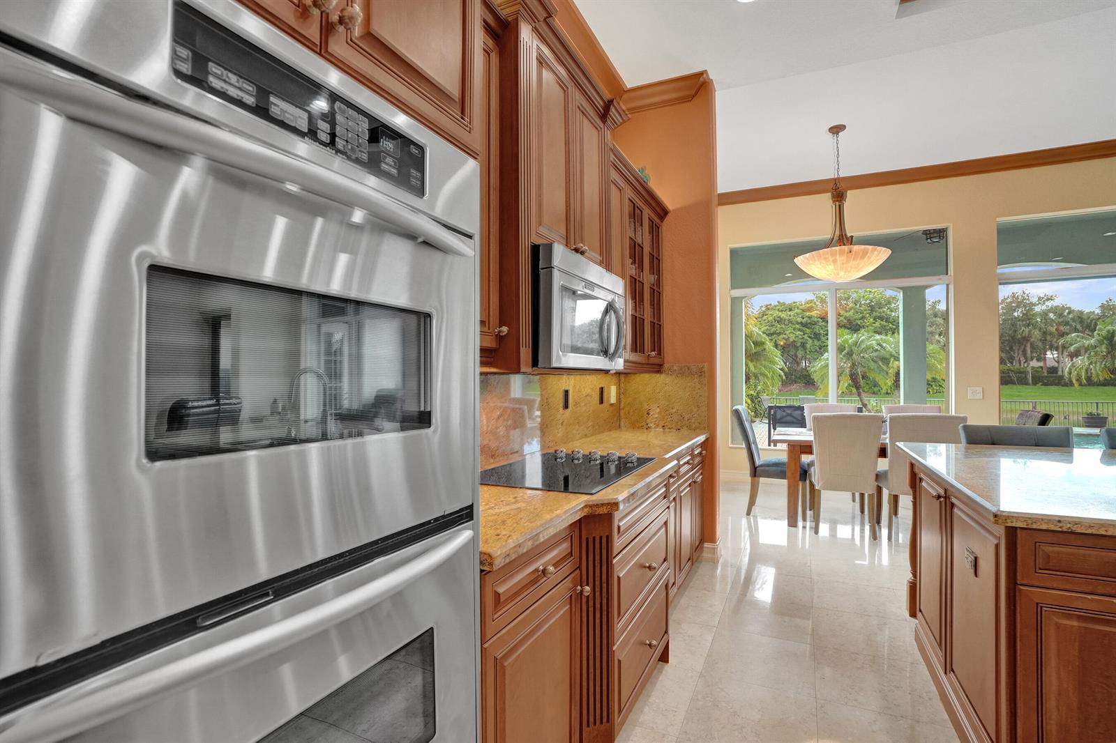 A kitchen features wood cabinets, granite countertops, stainless steel appliances, and a view of a patio — 12370 NW 80th Place, Parkland FL 33076, PARKLAND, FL