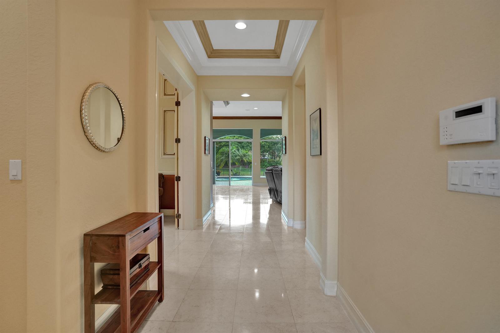 A tiled hallway leads toward a view of a backyard pool through sliding glass doors — 12370 NW 80th Place, Parkland FL 33076, PARKLAND, FL
