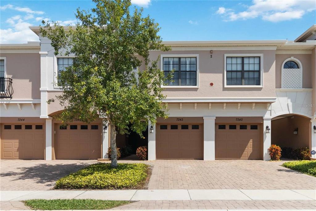 A row of three townhome garages with beige stucco walls and paved driveways — 7242 HAMILTON ROAD, BRADENTON, FL