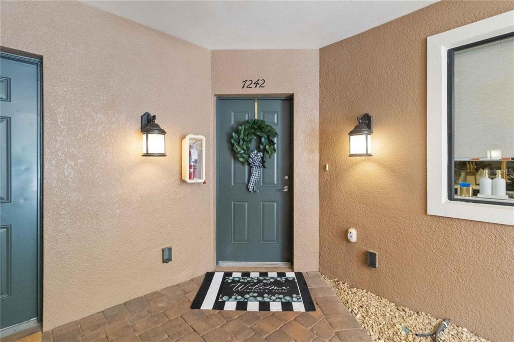An exterior entryway features a dark green door with a wreath, sconces, and stone pavers — 7242 HAMILTON ROAD, BRADENTON, FL