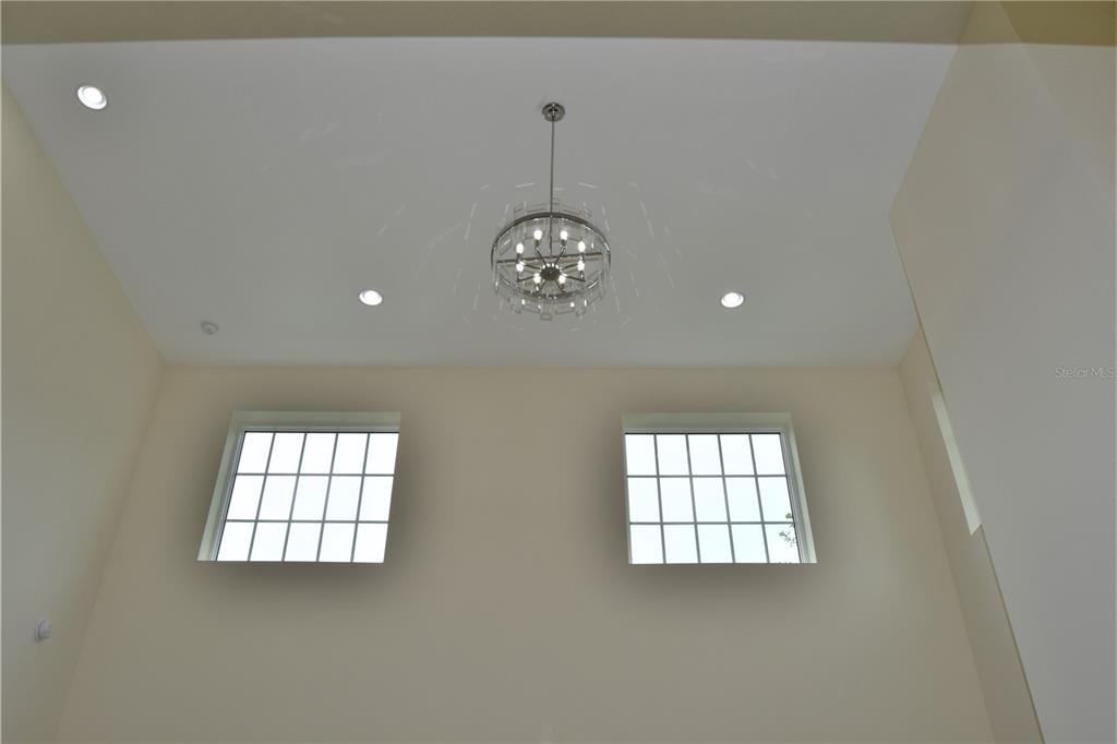A high-ceilinged room features a central crystal chandelier, recessed lighting, and two square windows — 6706 BURLINGTON AVENUE, ST PETERSBURG, FL