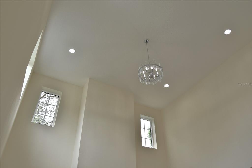 A high-ceilinged room features a modern crystal chandelier, recessed lighting, and two tall windows — 6706 BURLINGTON AVENUE, ST PETERSBURG, FL