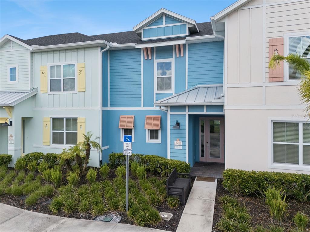 A multi-story townhouse exterior features blue and white siding with a front entrance and landscaping — 8201 SURF STREET, KISSIMMEE, FL