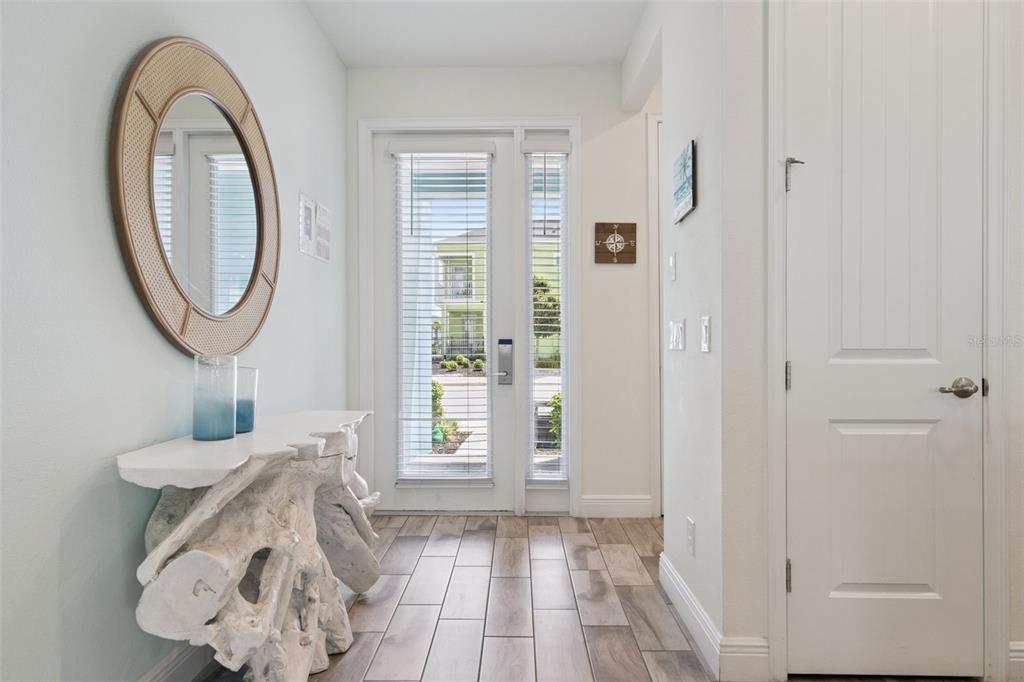 An entryway features a driftwood console table, a round mirror, and a glass-paneled front door — 8201 SURF STREET, KISSIMMEE, FL