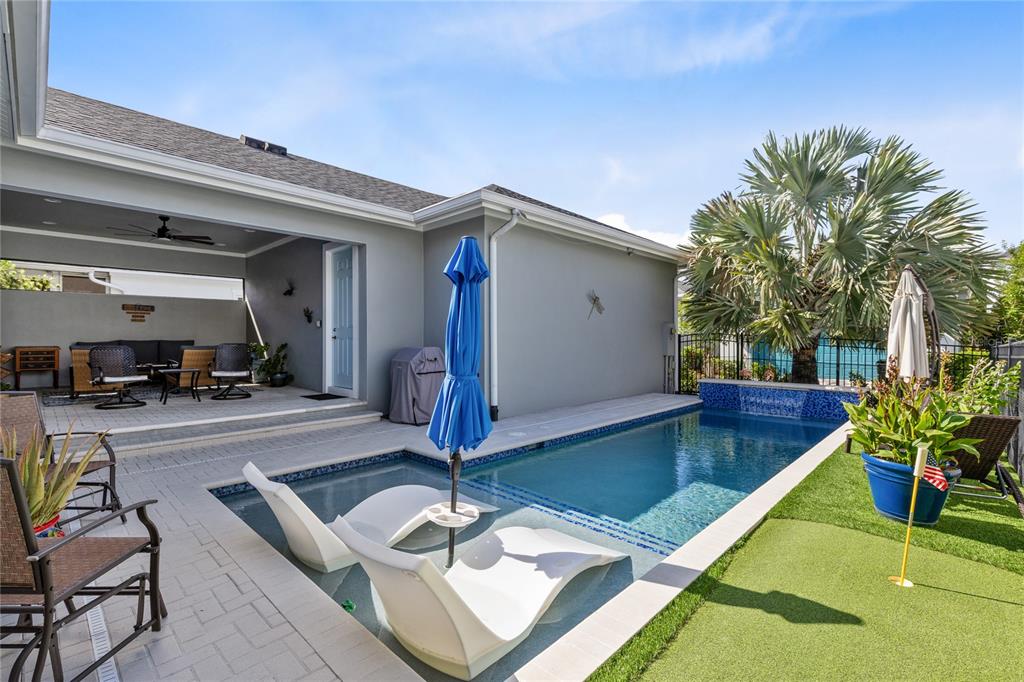 A backyard patio features a covered seating area, a swimming pool, and a putting green — 7838 DAUSSET STREET, ORLANDO, FL
