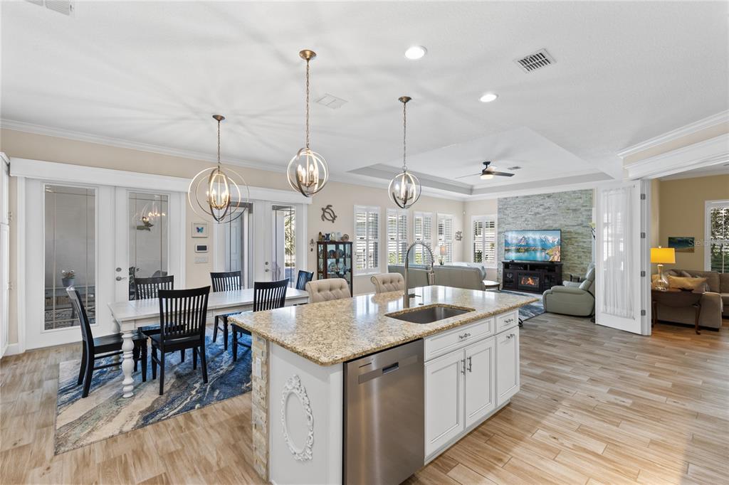 An open-concept kitchen and dining area features a granite-topped island and light wood flooring — 7838 DAUSSET STREET, ORLANDO, FL