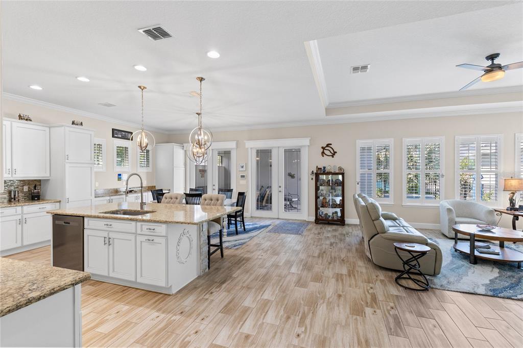 A bright, open-concept kitchen and living area featuring white cabinetry, granite countertops, and wood-look flooring — 7838 DAUSSET STREET, ORLANDO, FL