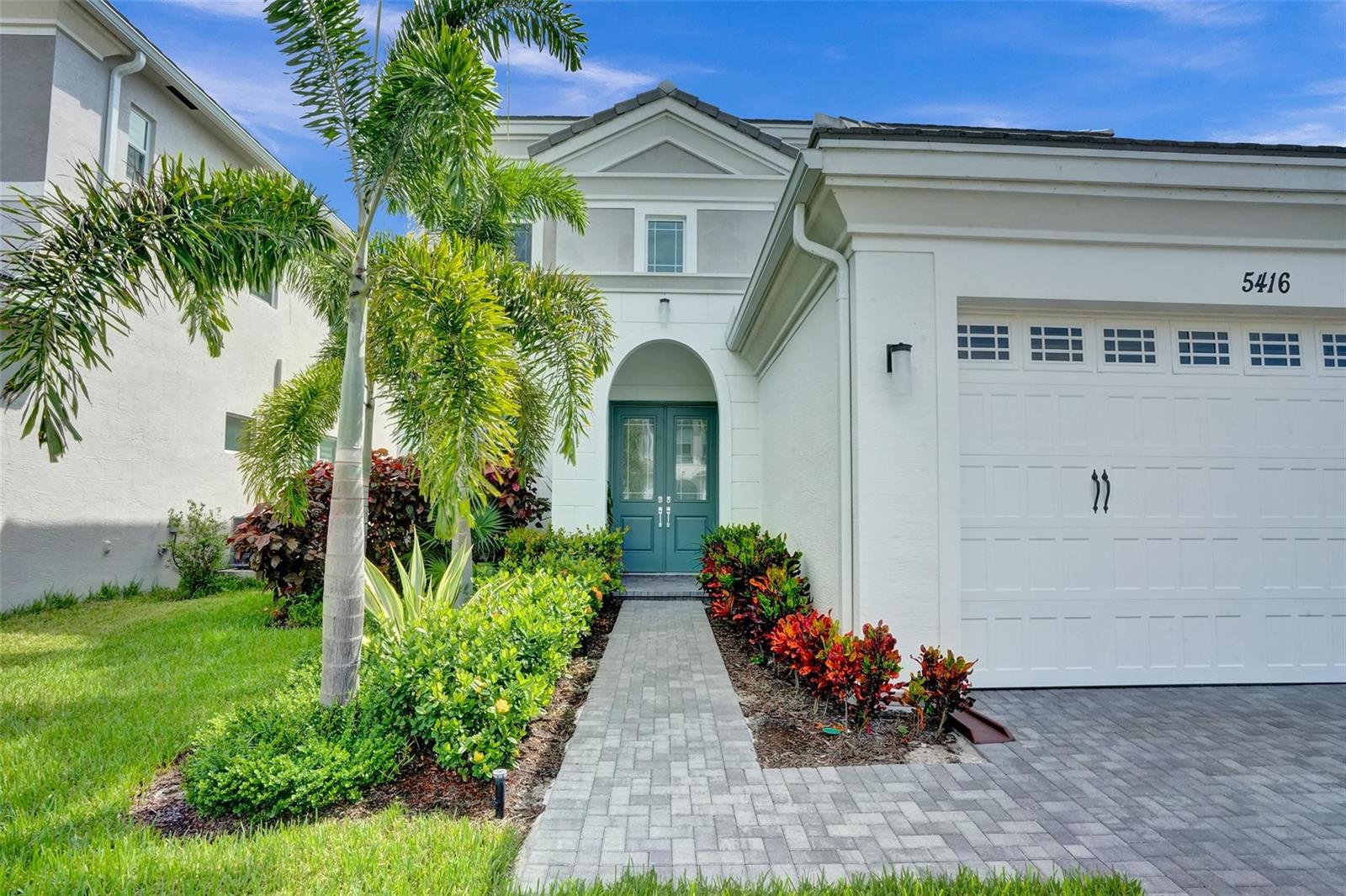 A two-story house exterior features a teal double front door, a paved walkway, and landscaping — 5416 Macoon Way, FL 33470, FL
