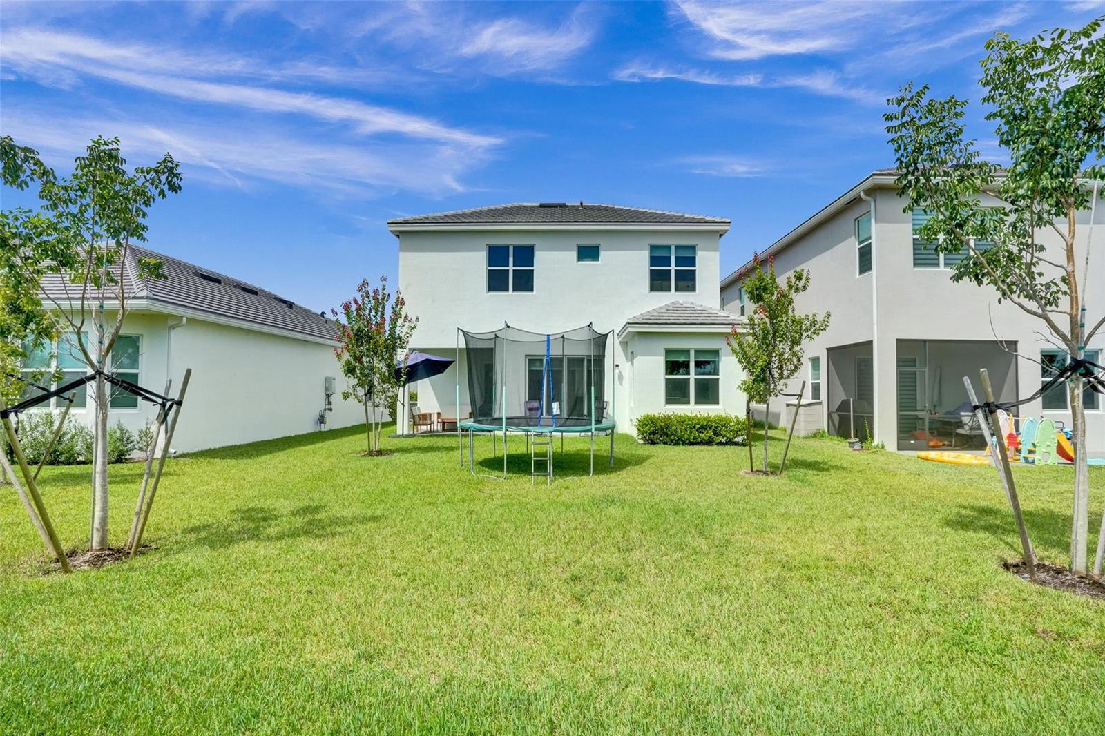 The backyard of a two-story house features a trampoline on a green lawn — 5416 Macoon Way, FL 33470, FL