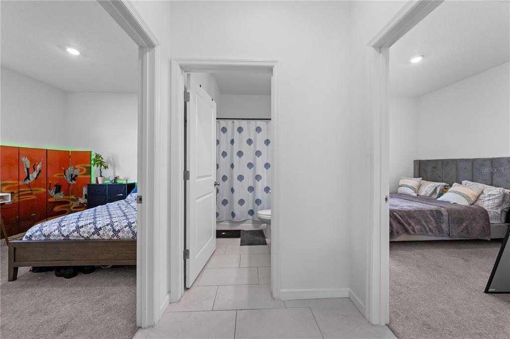 A hallway with light tile flooring leads to a bathroom between two carpeted bedrooms — 425 SILVER PALM DRIVE, HAINES CITY, FL