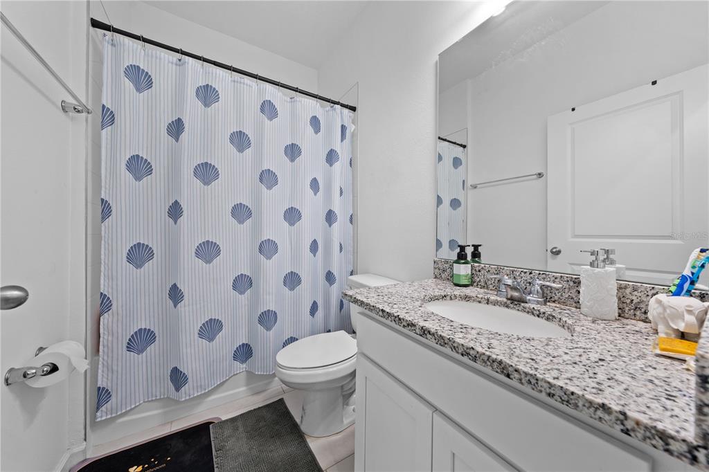 A bathroom features a white vanity with a granite countertop, toilet, and seashell-patterned shower curtain — 425 SILVER PALM DRIVE, HAINES CITY, FL