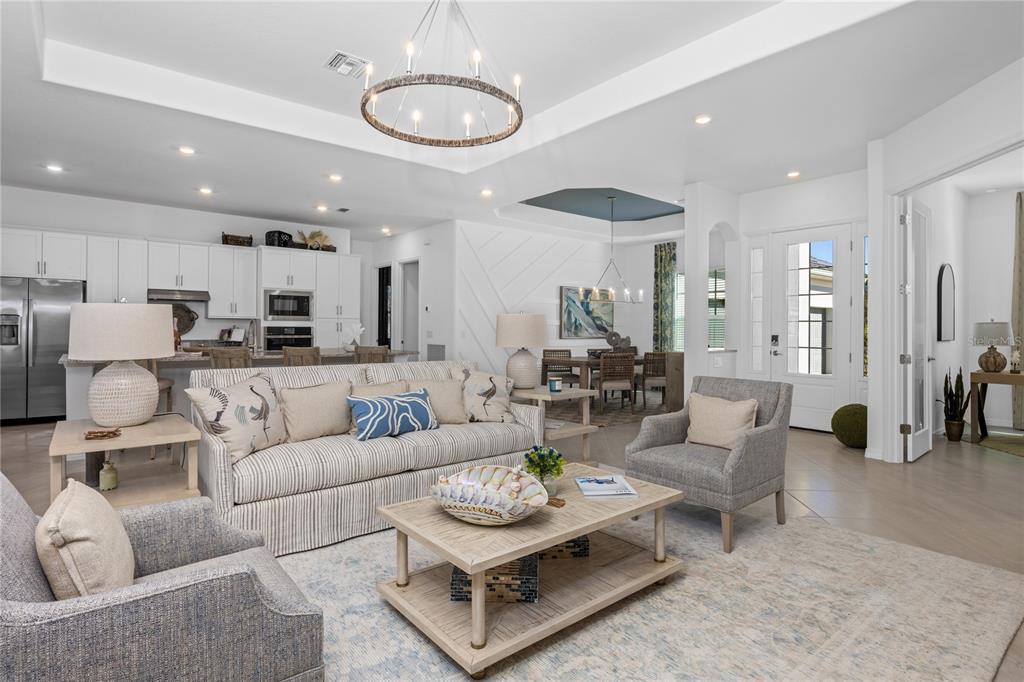 An open-concept living room features a striped sofa, two armchairs, and a kitchen in back — 18845 CHERRYSTONE WAY, LAKEWOOD RANCH, FL
